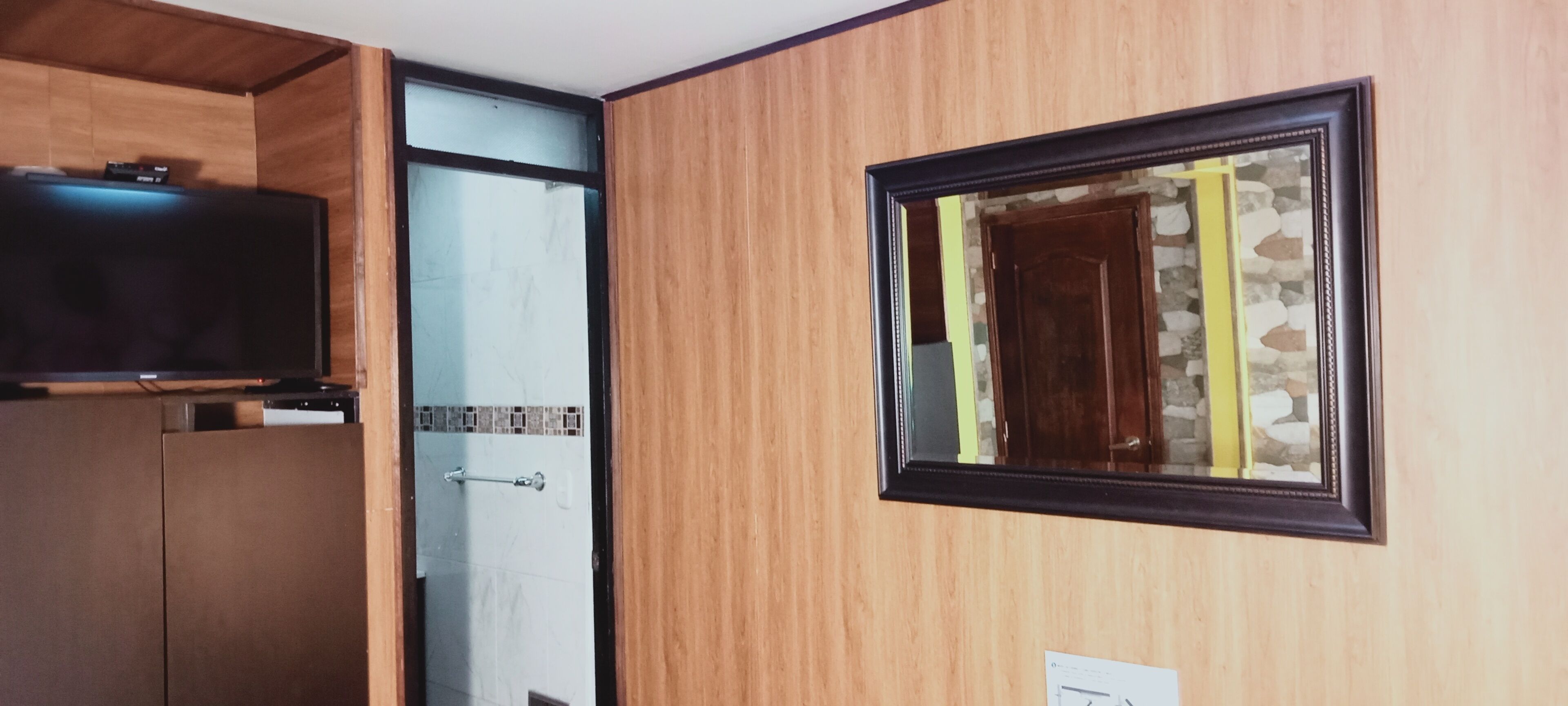 Una habitación con paneles de madera, un cuadro enmarco, una puerta y un televisor sobre un mueble.