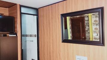 Una habitación con paneles de madera, un cuadro enmarco, una puerta y un televisor sobre un mueble.