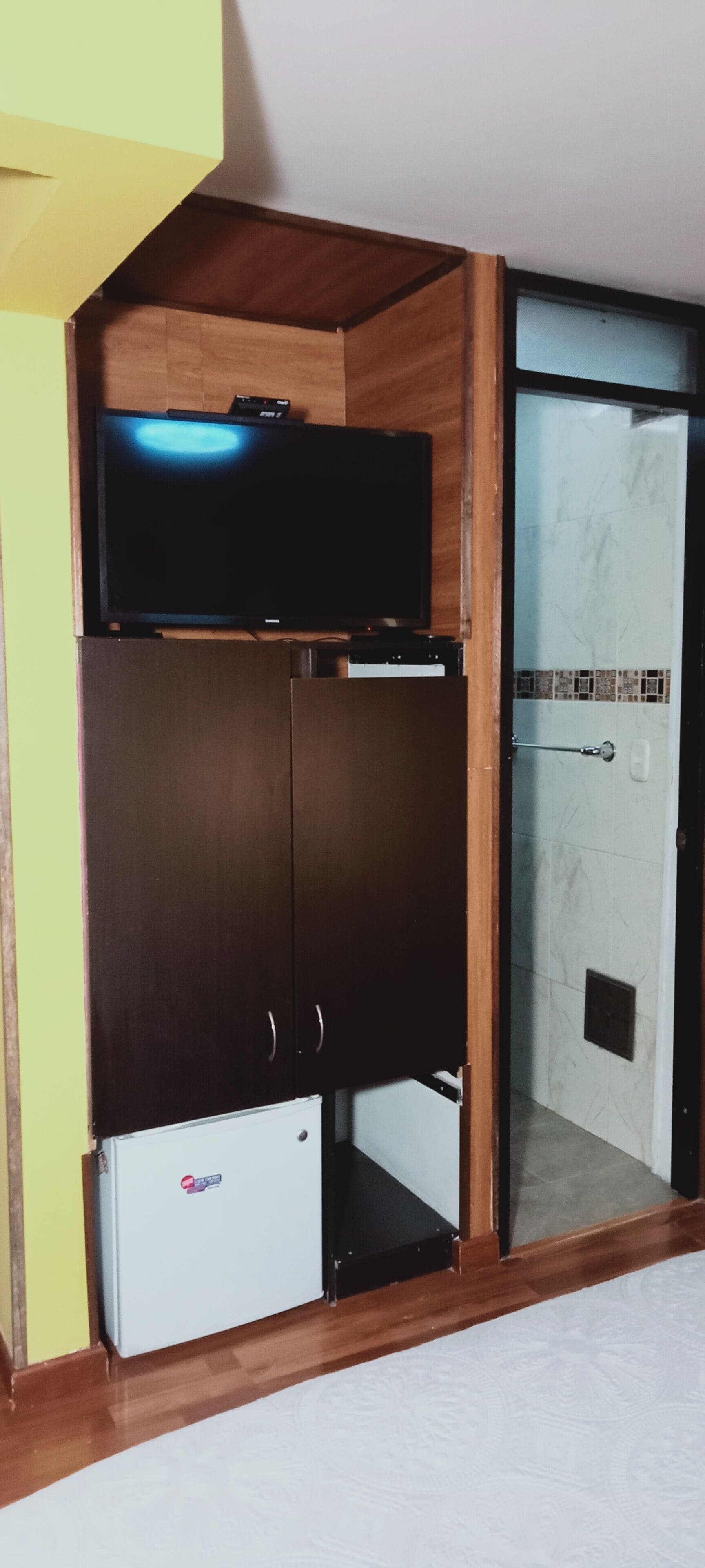 Habitación con televisor integrado, armario y un refrigerador pequeño.