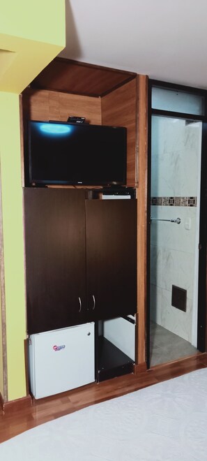 Habitación con televisor integrado, armario y un refrigerador pequeño.
