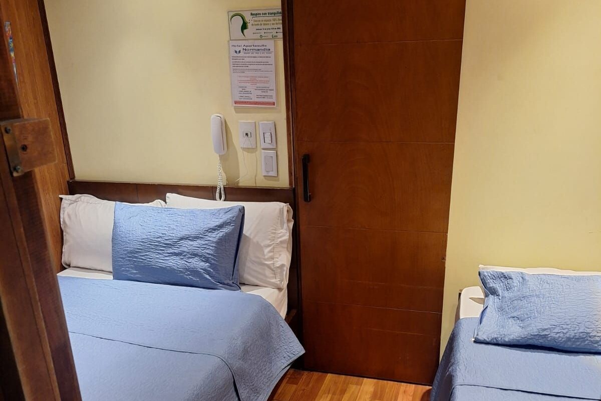 A hotel room with two beds, wooden flooring, a wooden door, and a wall-mounted phone.