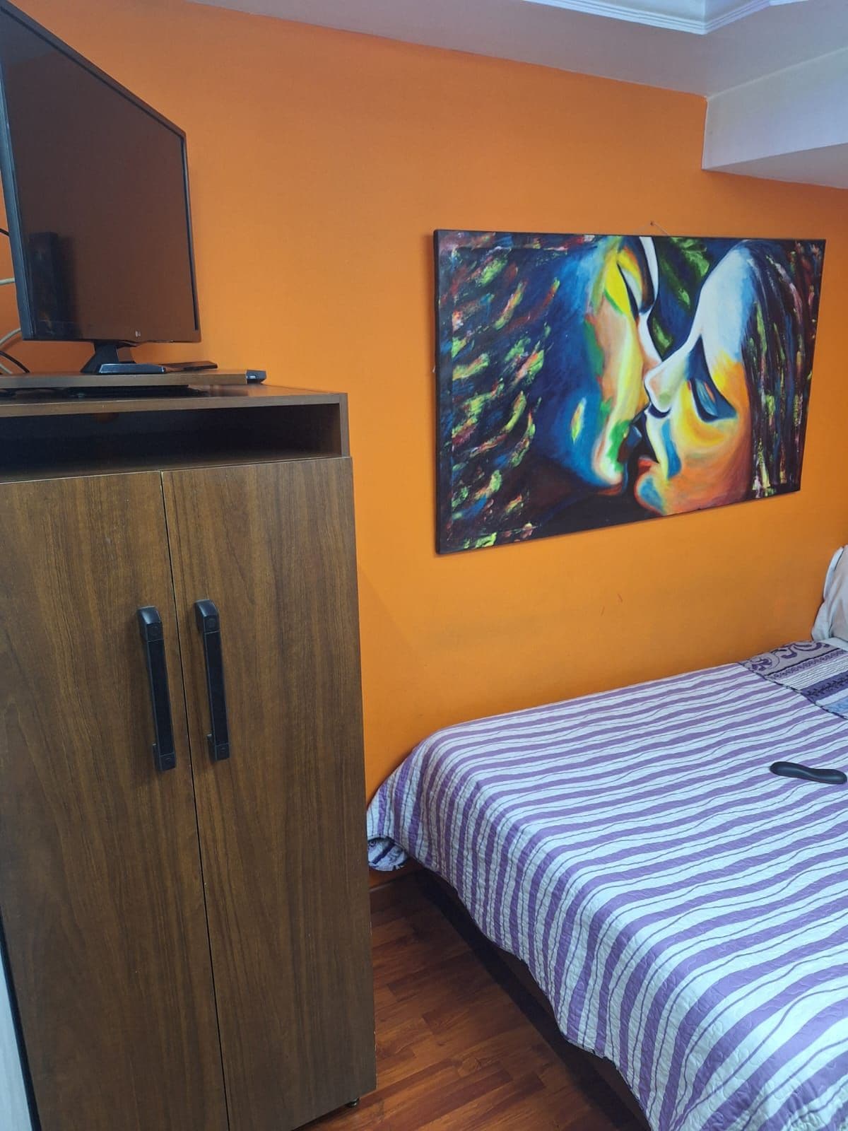 Ein Schlafzimmer mit einem Bett, einem Holzschrank und einem Bild an der Wand.