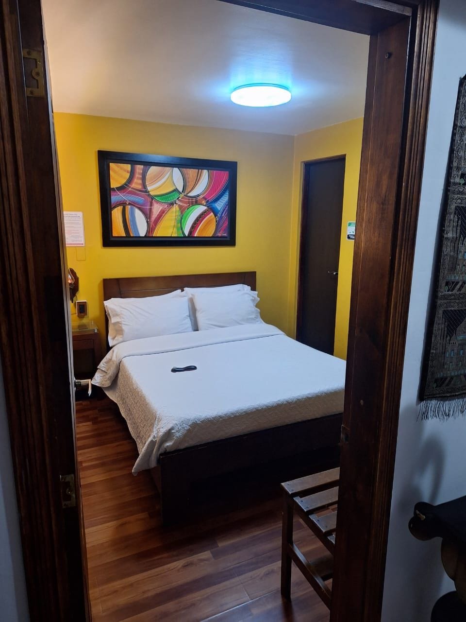 Ein Zimmer mit einem Bett, Holzboden, einem Wandbild und einer Tür.