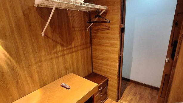 A compact room with a wooden floor, a small desk with drawers, a hanging clothes rack, and a door. - Hotel Apartasuite Normandia (Bogotá)