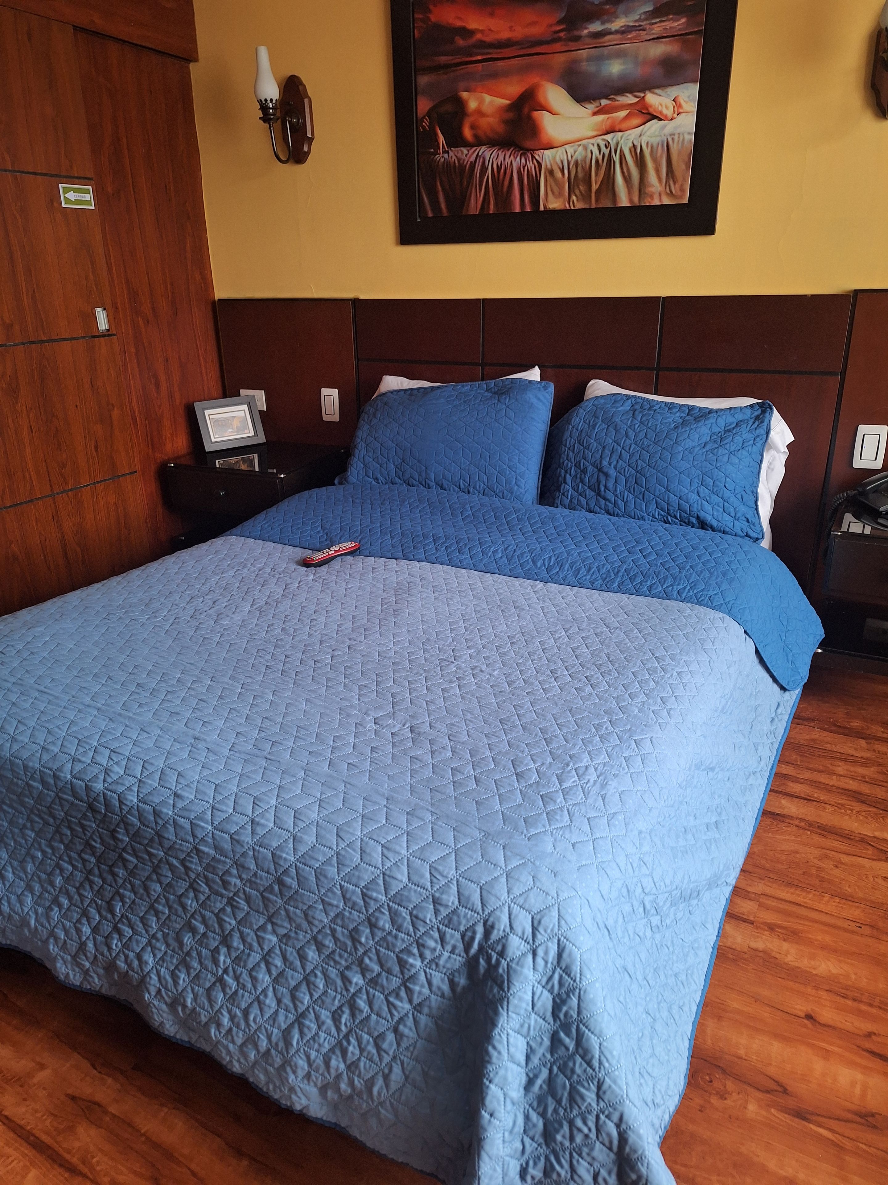 Una habitación de hotel con una cama grande, una mesita de noche, un cuadro en la pared y un armario de madera.