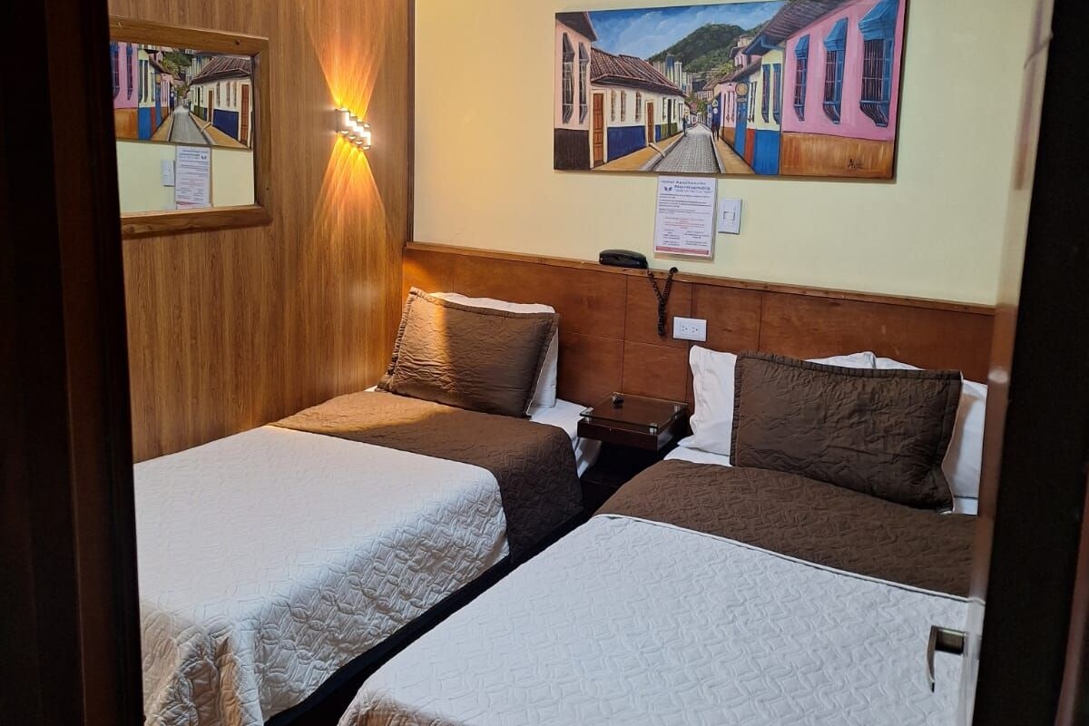 A hotel room with two beds, a wooden headboard, a ceiling with a light fixture, and two paintings on the wall.