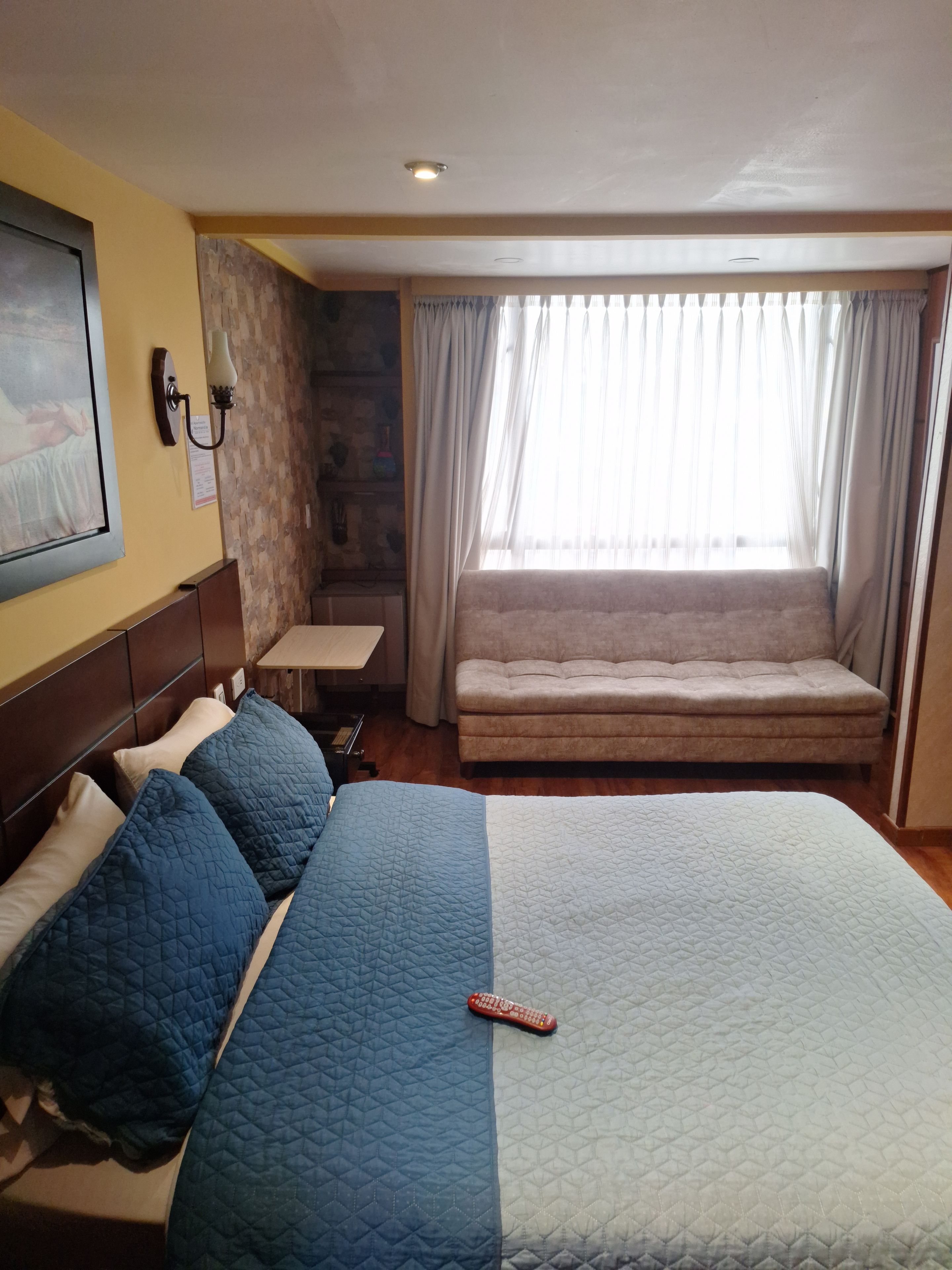 Habitación de hotel con una cama grande, una mesita de noche, una lámpara, una ventana con cortinas y una obra de arte colgada en la pared.