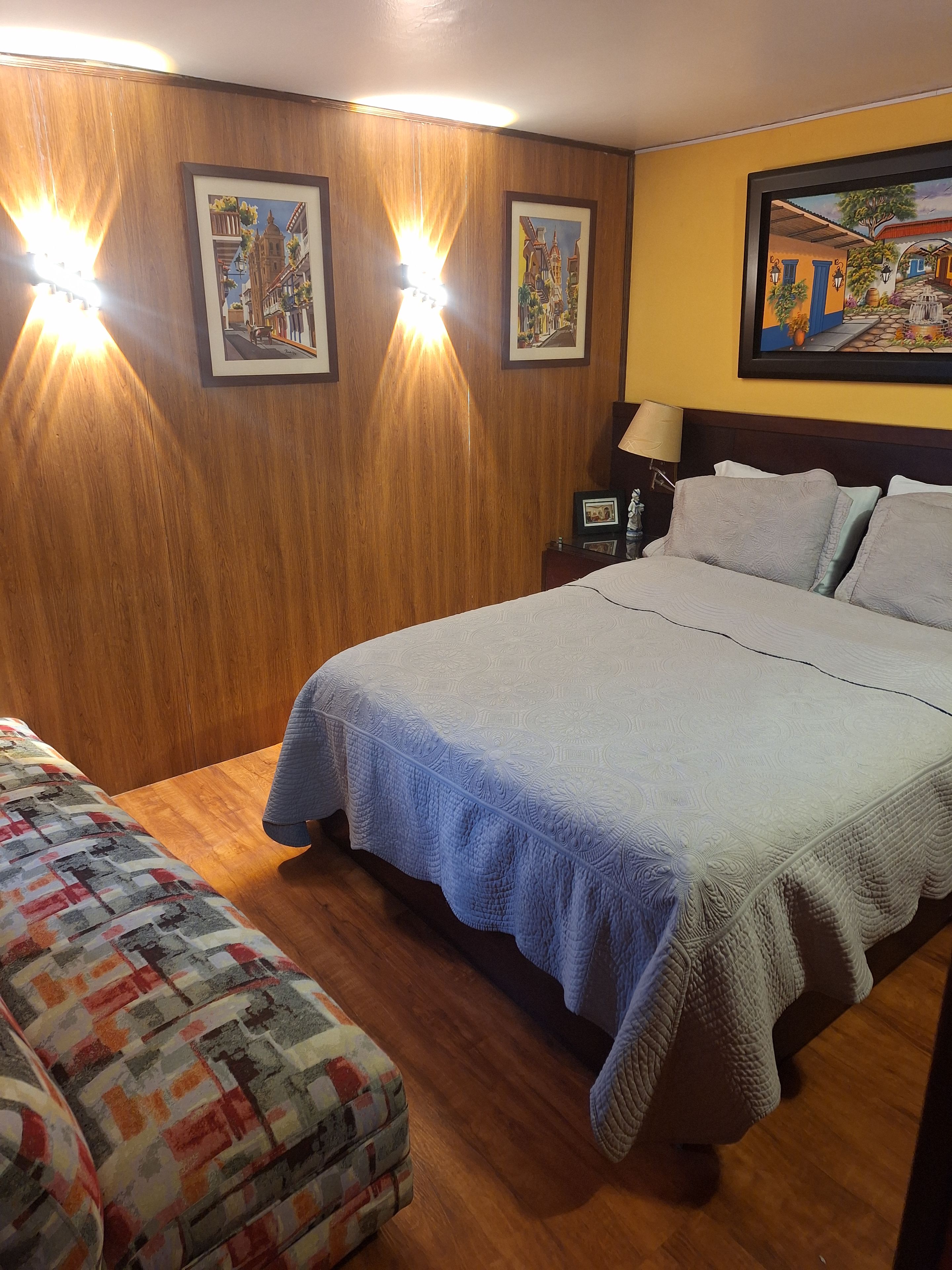A hotel room with a large bed, a bedside table with a lamp, and two framed pictures on the wall.