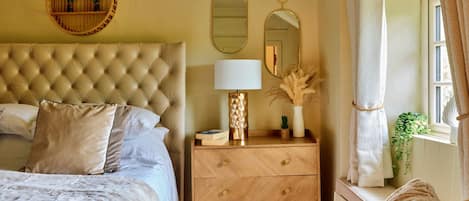 A bedroom with a tufted headboard, a bedside table with a lamp, and a mirror.
