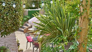 An outdoor patio area with a seating arrangement, potted plants, and string lights. - Charming Cottage for 4 in Dorset (Brixham)