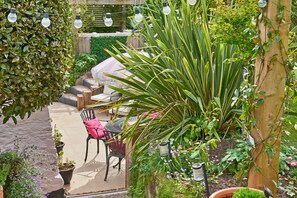 An outdoor patio area with a seating arrangement, potted plants, and string lights. - Charming Cottage for 4 in Dorset (Brixham)