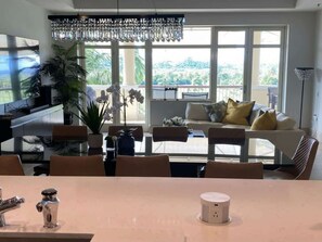 A modern living room with a dining area, large windows, a chandelier, and a view of the outdoors. - Villa Lakeview - Plantation - Dorado Beach Resort (Dorado)
