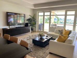 Ein modernes Wohnzimmer mit Flachbildfernseher, Essbereich und einer Couch mit gelben Kissen.