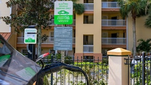 Ein Parkplatz mit Ladestationen für Elektrofahrzeuge, ein Schild, das die Parkplatznutzung für Elektrofahrzeuge kennzeichnet, und ein mehrstöckiges Gebäude im Hintergrund.