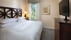 A neatly made bed with white linens, a wooden headboard, a bedside lamp, a framed picture on the wall, and a television on a wooden cabinet. - Orlando Getaway: 1BR Villa in the Cascades Section – Sheraton Vistana (Orlando)