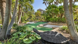Um jardim tropical com piscina, palmeiras e uma grande escultura de cágado.