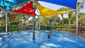 Ein Spielbereich im Freien mit einem blauen Pool, umgeben von einem Zaun, unter einer Überdachung mit roten, gelben und blauen Paneelen.