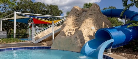 Un parque acuático con piscina, una formación rocosa y un tobogán de agua azul.