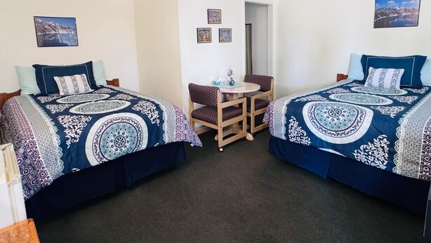 A room with two beds, a small table, and chairs. There are pictures on the walls. - GOLDEN WEST MOTEL (Klamath Falls)