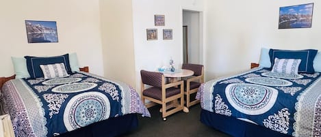 A room with two beds, a small table, and chairs. There are pictures on the walls.