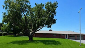 A building with a red brick exterior, a large tree in front, and a clear blue sky. - GOLDEN WEST MOTEL (Klamath Falls)