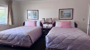A hotel room with two beds, a nightstand, a lamp, and two framed pictures on the wall.