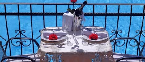 Ett bord dukat för två personer, med en flaska champagne, glas och röda rosor på en balkong med utsikt över en pool.