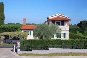 Ein zweistöckiges Haus mit rotem Ziegeldach, Schornstein und grünen Fensterläden.
