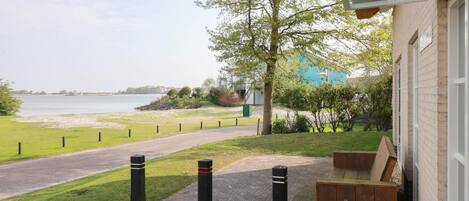 A view of a building with a paved pathway leading to a grassy area and a body of water.