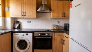 Una cucina con mobili in legno, lavatrice, forno e microonde.