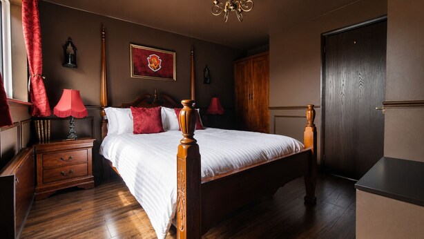 Una camera da letto con un letto a baldacchino, comodini in legno, una lampada rossa, un quadro incorniciato appeso al muro e un armadio.