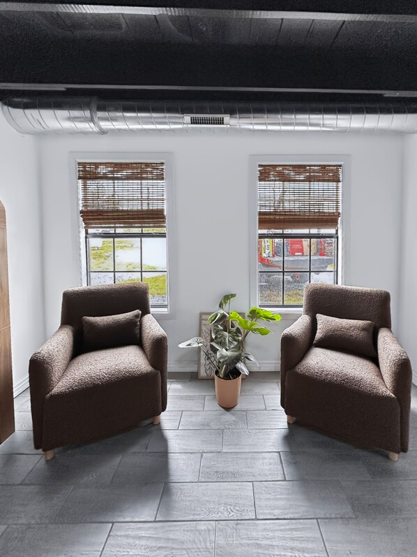 A room with two brown armchairs, a potted plant, and a window with blinds.