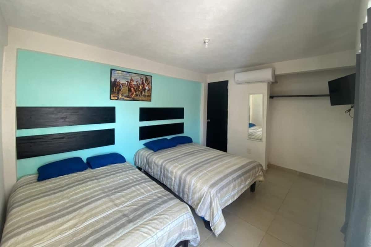 Una habitación con dos camas, un cuadro en la pared, un aire acondicionado y un televisor.