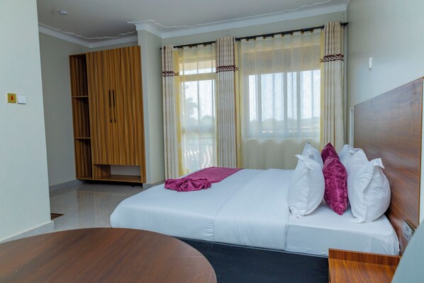 A hotel room with a bed, a wooden wardrobe, and a window with curtains.
