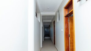 A corridor with white walls, a tiled floor, and a wooden door labeled 'WASHROOM'. - Hotel Amani Limited (Jinja)