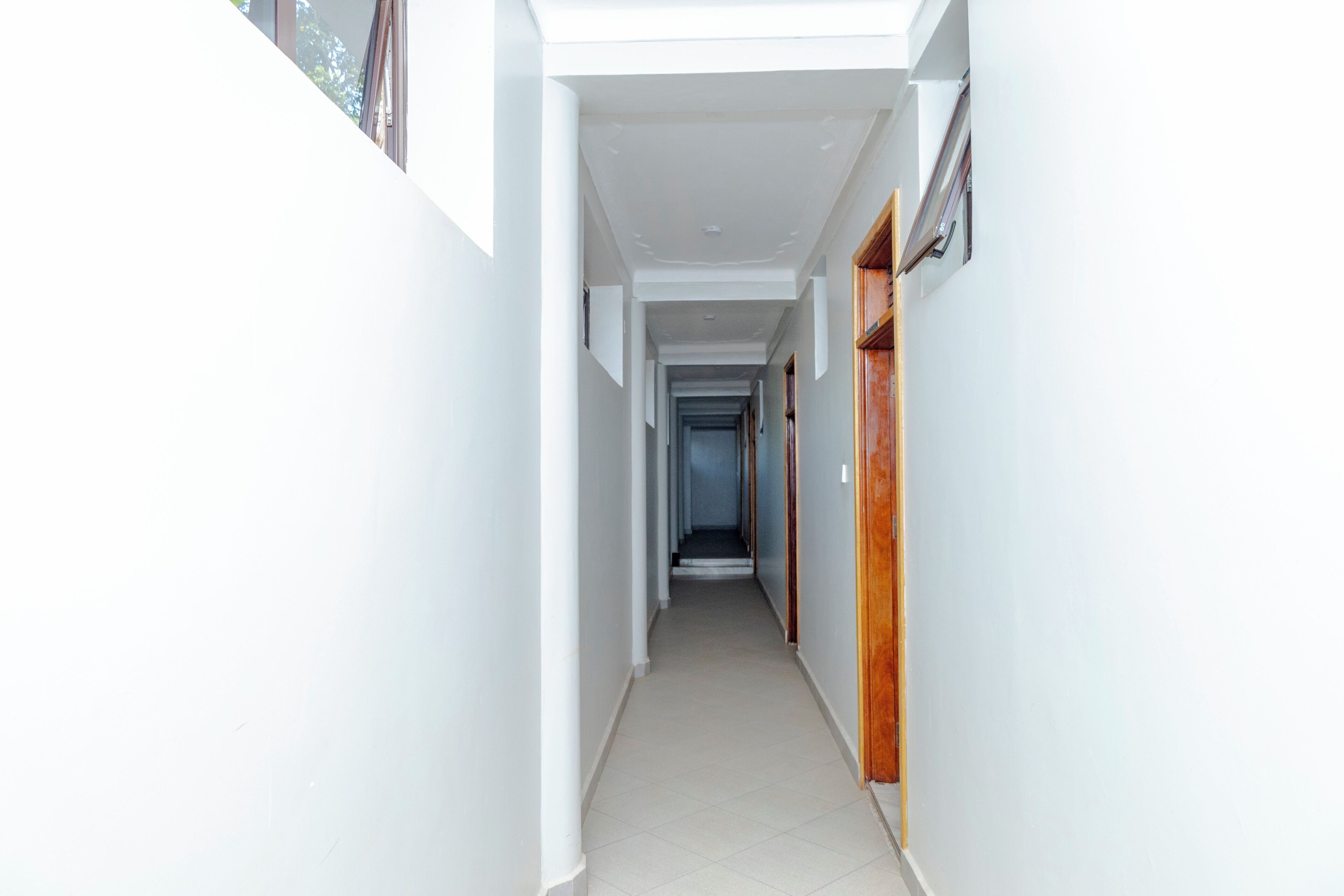 A narrow hallway with white walls and a tiled floor, leading to a door at the end.
