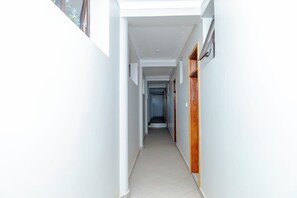 A narrow hallway with white walls and a tiled floor, leading to a door at the end.