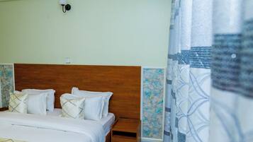 Quarto com cabeceira de madeira, cama com roupa de cama branca, mesa de cabeceira e luminária fixada na parede.