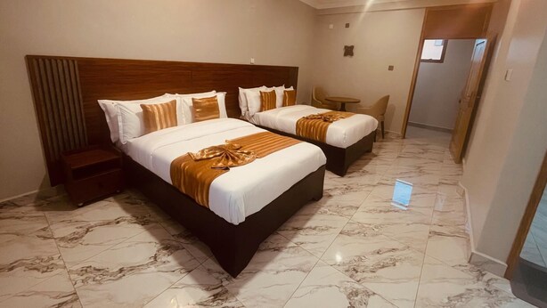 A hotel room with two beds, a small table, and a chair. - Hotel Amani Limited (Jinja)