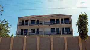 A multi-story residential building with balconies, a flat roof, and a stone wall in front. - Hotel Amani Limited (Jinja)