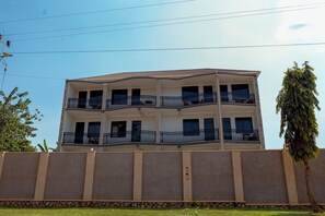 A multi-story residential building with balconies, a flat roof, and a stone wall in front.
