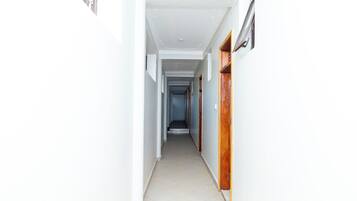 A narrow hallway with white walls and a tiled floor, leading to a door at the end.
