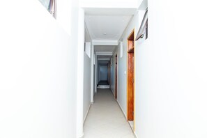 A narrow hallway with white walls and a tiled floor, leading to a door at the end.