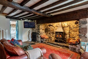 A cozy living room with a stone fireplace, leather sofas, and a television mounted on the wall. - Cottage in Snowdonia National Park (Dolgellau)