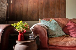 A leather sofa with a patterned pillow and a red vase with flowers. - Cottage in Snowdonia National Park (Dolgellau)
