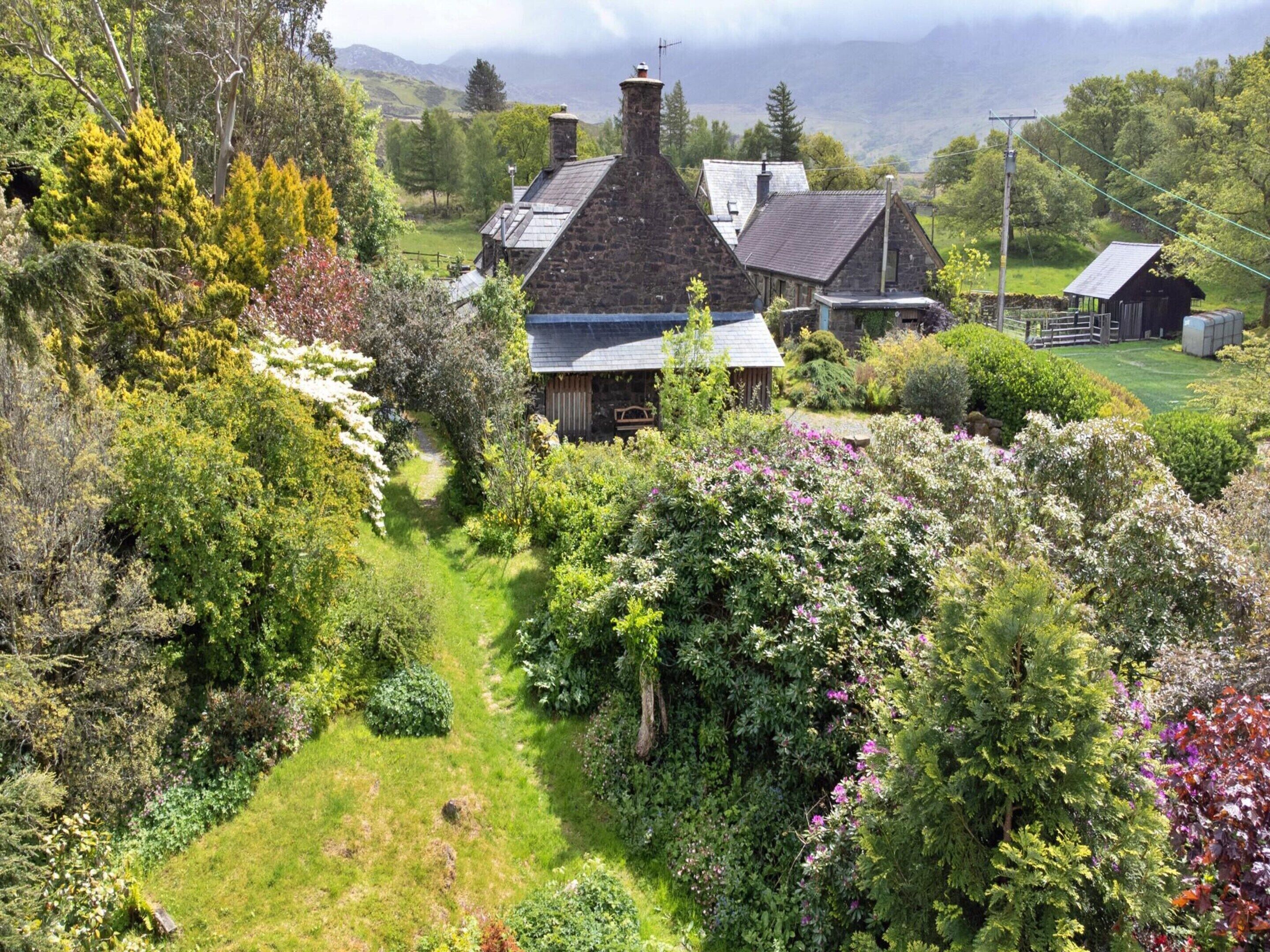 Ein Haus aus Stein mit geneigtem Dach, umgeben von üppiger Vegetation und einem klaren Weg zum Eingang.
