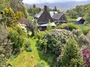 A stone house with a sloped roof surrounded by lush greenery and a clear path leading to the entrance. - Cottage in Snowdonia National Park (Dolgellau)