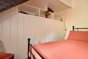 Une chambre à coucher avec un lit, une armoire blanche et une étagère contenant des livres et un vase.