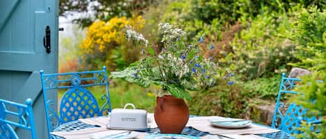 A round table with a vase of flowers, a butter container, and a book titled 'ISIGNY-MÈRE' with a plate and a spoon on it.