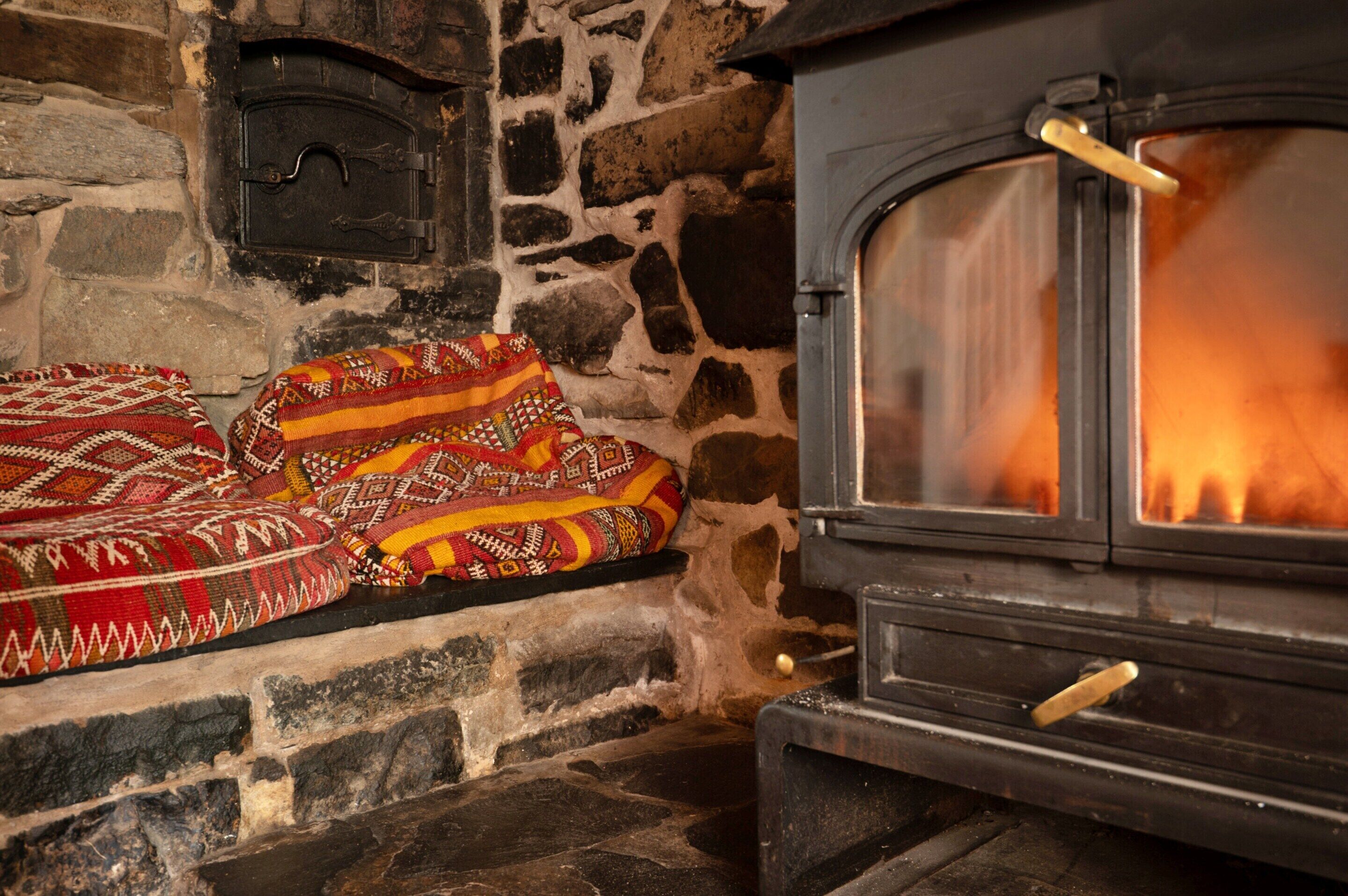 A stone fireplace with a fire, a bench with a patterned blanket, and a rustic wooden door.